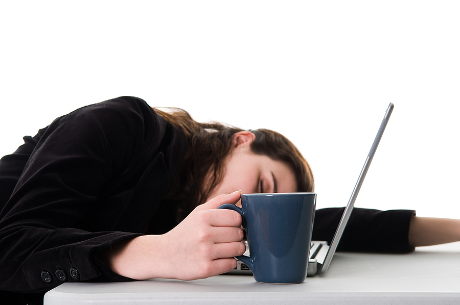 A lady sleeping in front of a computer with a mug of coffee and a computer